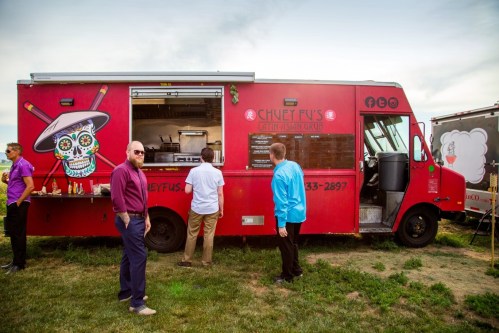 A vibrant food truck with a colorful design, serving Latin and Asian cuisine, with people interacting nearby.