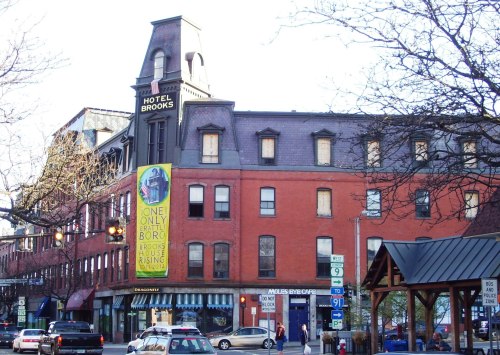 Historic Hotel Brooks building with a prominent sign, featuring a colorful banner, surrounded by trees and street elements.