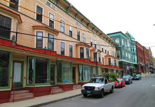 A street view of colorful historic buildings with shops and parked cars in a small town.