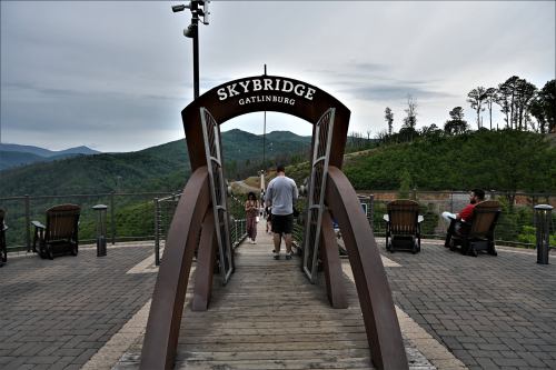 A wooden bridge with an archway labeled "SkyBridge" leads into a scenic mountain landscape in Gatlinburg.