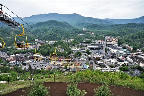 A scenic view from a chairlift overlooking a mountain town surrounded by lush greenery and distant mountains.