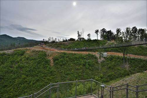 A scenic view of a winding path through green hills under a cloudy sky, with trees in the background.