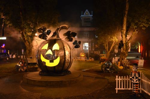 A large, glowing jack-o'-lantern surrounded by Halloween decorations in a foggy night scene.