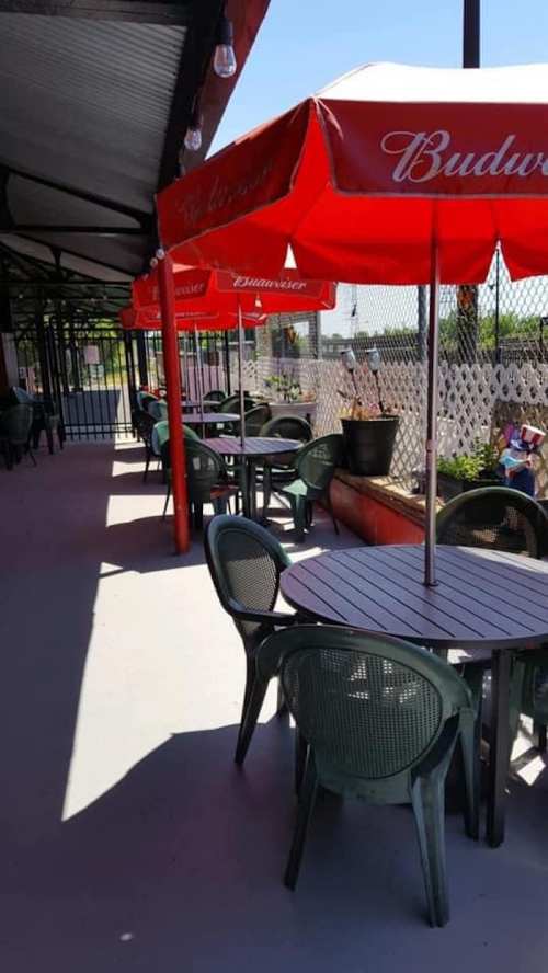 Outdoor seating area with green chairs and tables, shaded by red umbrellas, along a walkway.