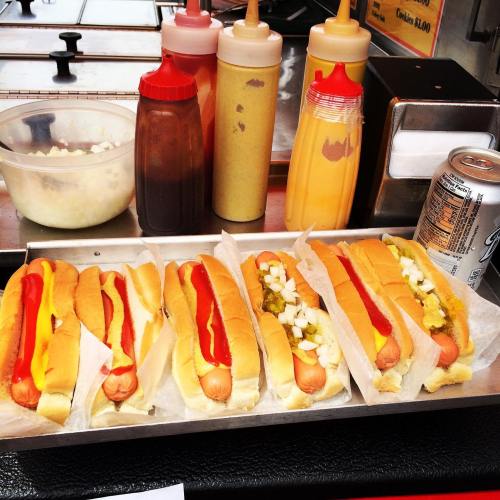 A tray of hot dogs with mustard, ketchup, and onions, alongside condiments and a soda can.