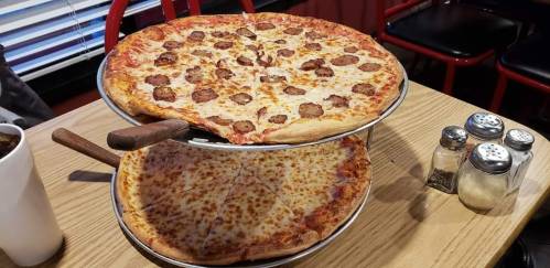 A two-tier pizza stand featuring a pepperoni pizza on top and a cheese pizza below, set on a wooden table.