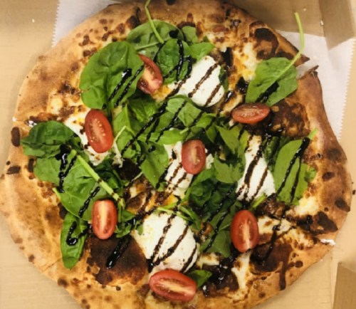 A freshly baked pizza topped with spinach, cherry tomatoes, and drizzled with balsamic glaze.
