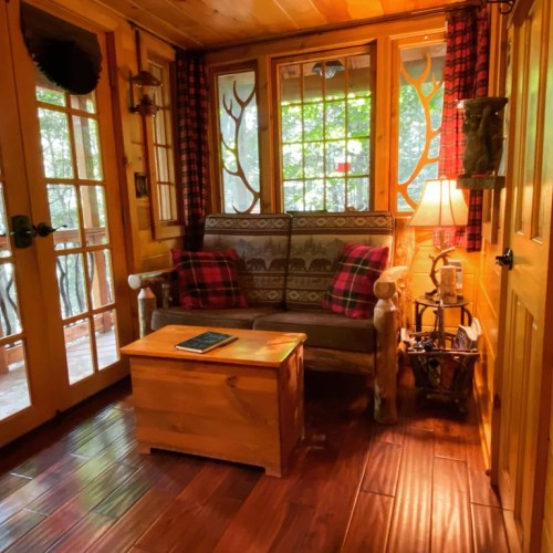 Cozy cabin interior with a wooden sofa, plaid pillows, a coffee table, and large windows letting in natural light.