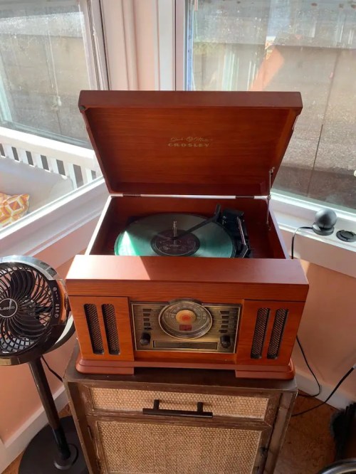 A vintage wooden record player with a green vinyl record, placed near a window and a small fan.