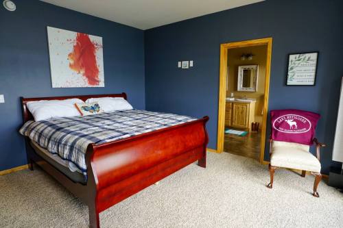 Cozy bedroom with a wooden sleigh bed, plaid bedding, and a chair, featuring blue walls and a bathroom doorway.