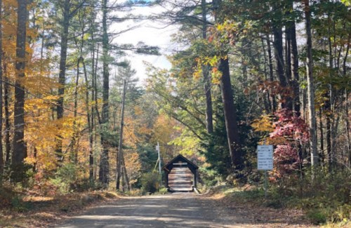 A dirt road leads to a covered bridge surrounded by colorful autumn trees.