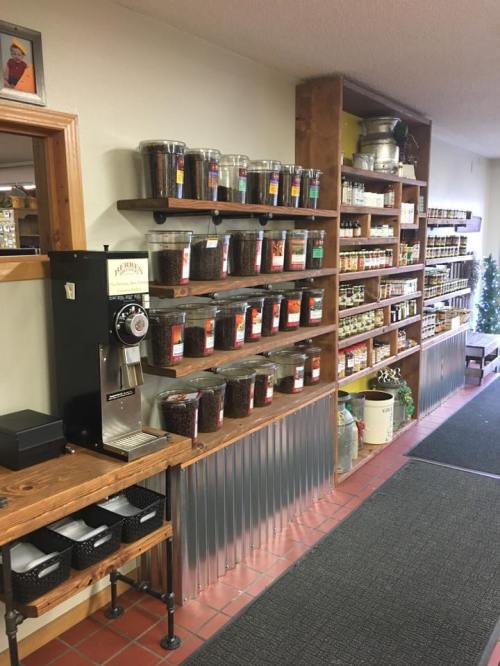 A cozy store interior featuring shelves of jars with various spices and a coffee grinder on a wooden counter.