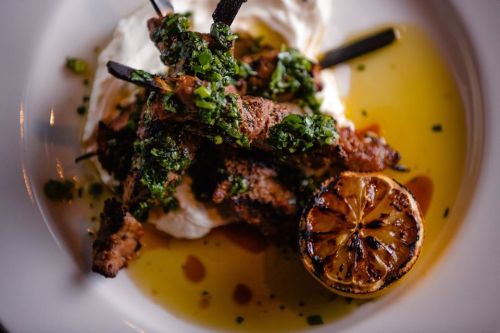 Grilled skewers topped with green herbs, served on creamy sauce with a charred lemon half on the side.