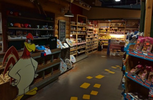 A cozy store aisle with shelves of goods, a cartoon chicken cutout, and a path marked by yellow footprints.