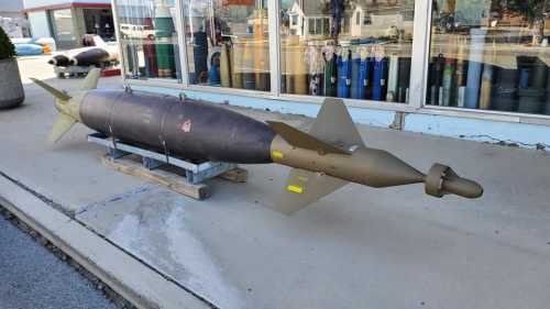 A large military bomb displayed on a concrete surface outside a store, with various colors and a streamlined design.