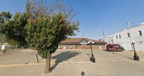 A brick building with a sign reading "JAG" surrounded by trees and street lamps on a clear day.