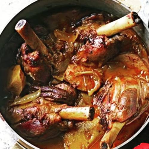 A pot filled with braised meat shanks in a rich, savory sauce with herbs and spices.