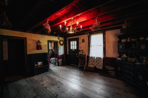 Cozy interior of a rustic room with wooden floors, red ceiling beams, and vintage decor, illuminated by a chandelier.