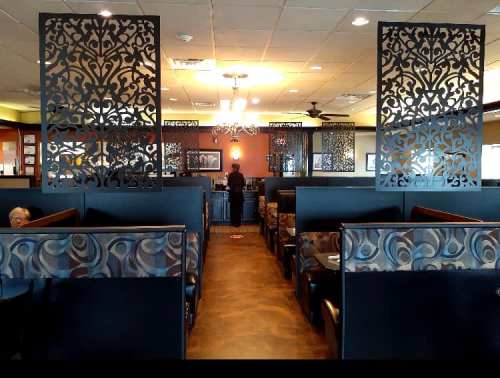 Interior of a restaurant featuring decorative partitions, booths, and a central service area. Warm lighting creates a cozy atmosphere.