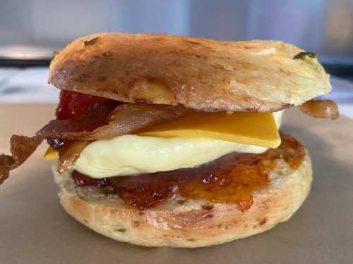 A biscuit sandwich with bacon, cheese, and a creamy spread, served on a paper tray.