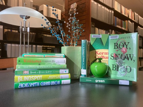 A table with green-themed books, a green vase, and decorative branches in a library setting.