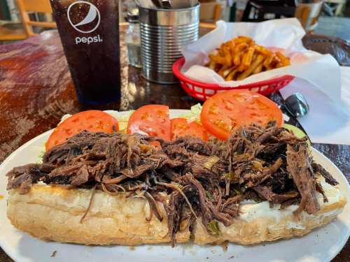 A hearty sandwich filled with shredded beef, topped with lettuce and tomato, served with a side of fries and a drink.
