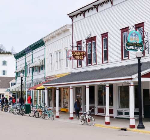 A charming street lined with shops, including Joann's Fudge and a hamburger restaurant, with bicycles parked outside.