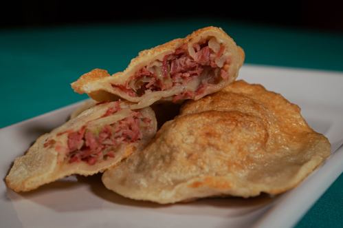 A close-up of golden-brown fried pastries filled with chopped meat and onions, served on a white plate.