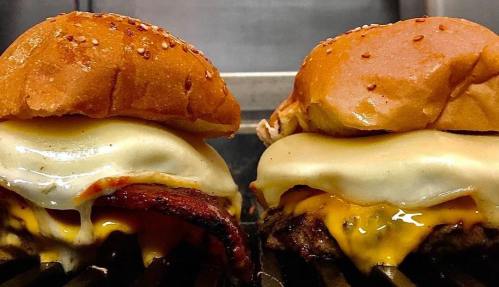 Two delicious burgers with melted cheese, crispy bacon, and sesame seed buns, sizzling on a grill.