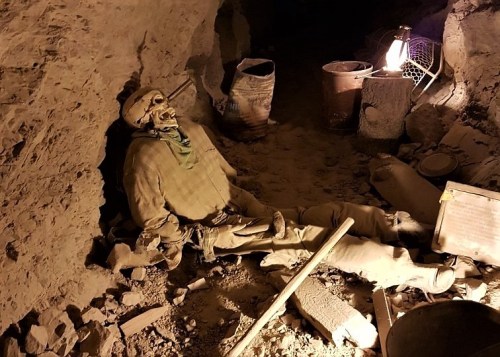A skeleton rests against a cave wall, surrounded by debris and dim lighting, suggesting an abandoned mining site.