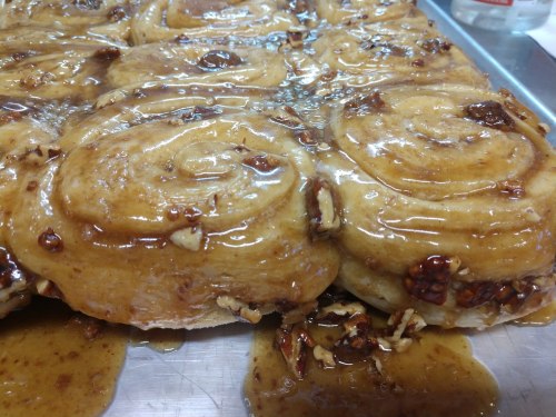 Close-up of sticky cinnamon rolls topped with a glossy caramel glaze and chopped nuts on a baking tray.