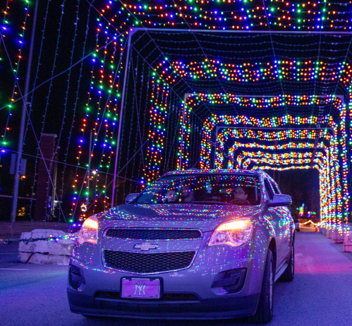 A silver car drives through a colorful, illuminated tunnel of lights at night.