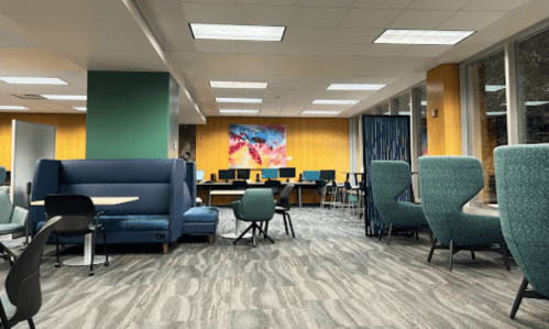 A modern study space with colorful artwork, seating areas, and computer stations in a well-lit room.