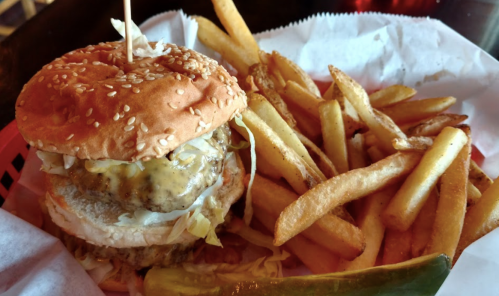 A sesame seed burger with lettuce and sauce, served with a side of golden French fries and a pickle.