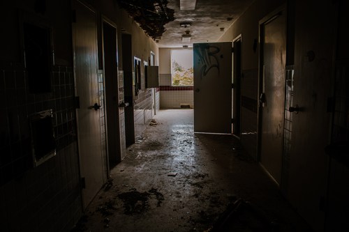 Dimly lit hallway in an abandoned building, with open doors and debris scattered on the floor.