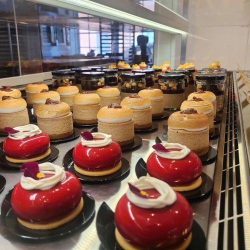A display of colorful desserts, including red dome cakes and layered pastries, arranged neatly on a shelf.