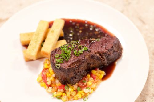 A plate featuring tender beef, corn salad, and crispy polenta sticks, drizzled with a rich sauce and garnished with green onions.