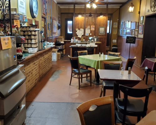 Interior of a cozy restaurant with tables, chairs, and a counter, featuring warm lighting and rustic decor.