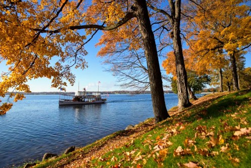A scenic view of a boat on a lake surrounded by vibrant autumn trees and fallen leaves.