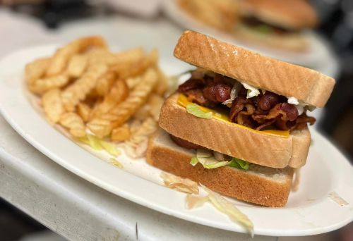 A stacked sandwich with bacon, cheese, and lettuce, served with a side of crinkle-cut fries on a white plate.
