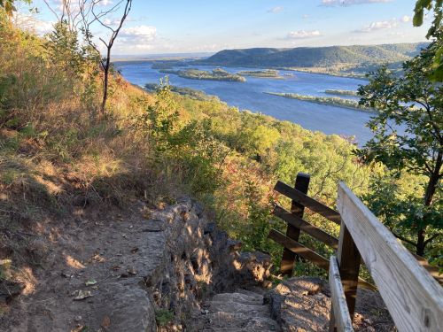 A scenic view of a river winding through green hills, with a wooden railing along a rocky path.