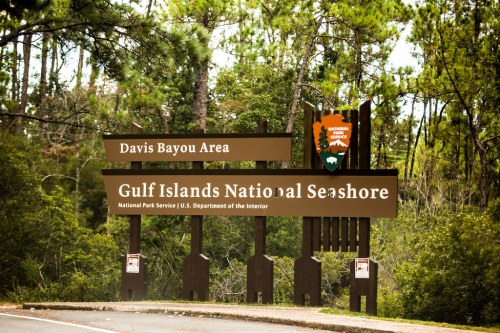 Sign for Davis Bayou Area at Gulf Islands National Seashore, surrounded by lush greenery and trees.