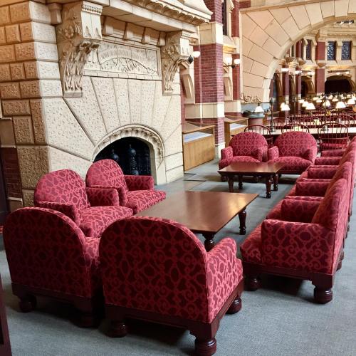 A cozy seating area with red upholstered chairs and a wooden table, set in a grand, architecturally detailed room.