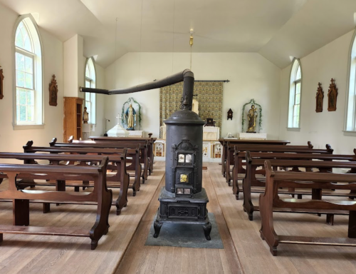Interior of a church featuring wooden pews, a central stove, and religious artwork on the walls.