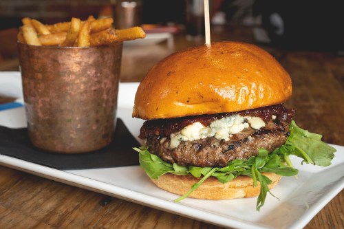 A juicy burger with blue cheese and lettuce, served with a side of crispy fries in a copper cup.