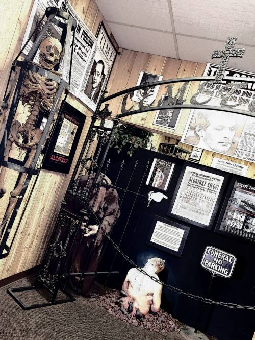 A museum display featuring a skeleton, vintage newspapers, and a sign reading "Funeral No Parking" in a themed room.