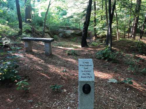 A serene forest scene with a stone bench and a monument inscribed with a quote about following God.