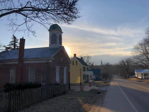 A quiet street scene at sunset, featuring a brick building with a bell tower and a yellow house nearby.