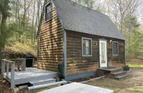 A small wooden cabin with a steep roof, front porch, and surrounded by trees in a natural setting.