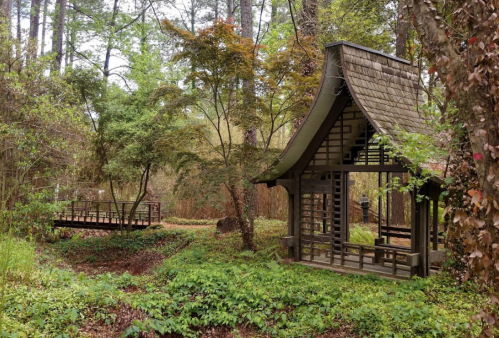A serene garden scene featuring a traditional wooden structure surrounded by lush greenery and trees.